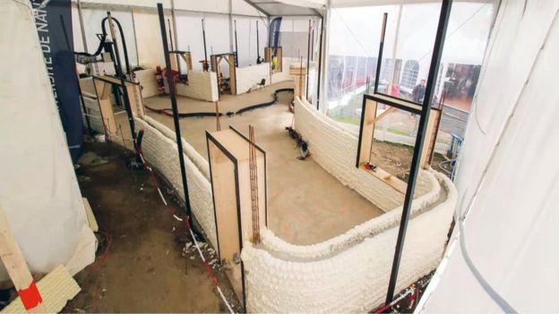 Stage 1 of construction for the 3D printed house. The space in-between the two printer blocks is filled with cement to form the wall. Photo via BBC.