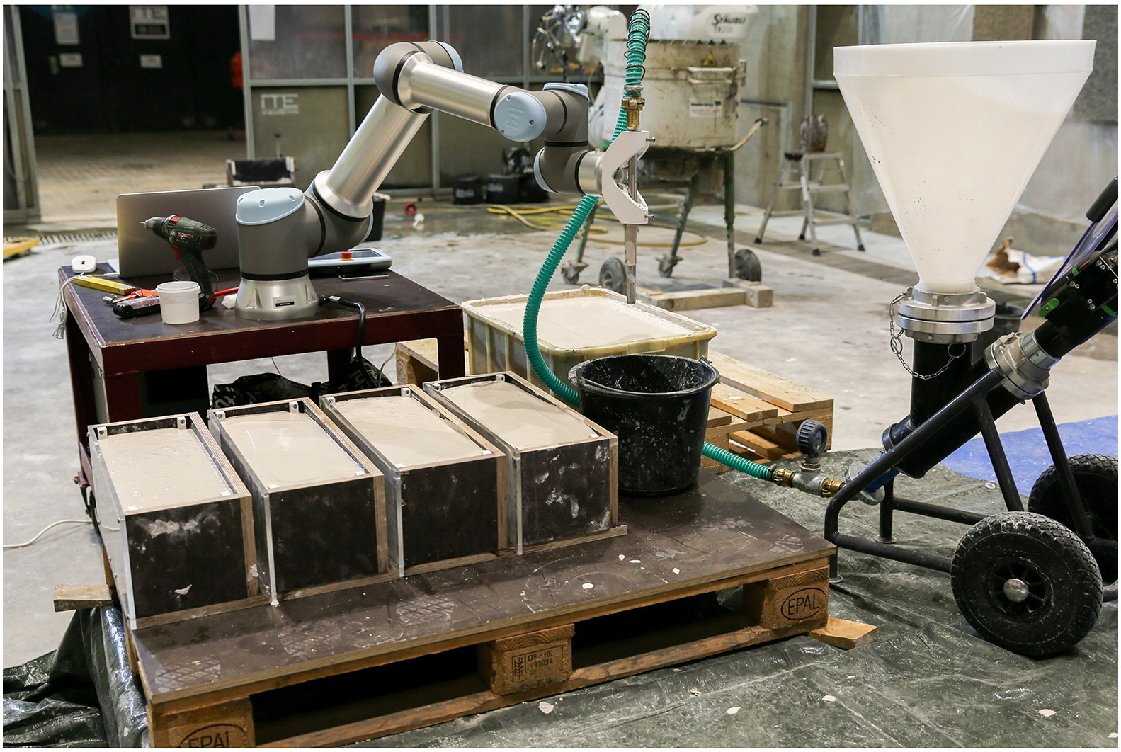 Injection 3D Concrete Printing setup: mixer, pump, robot, and formwork filled with ground limestone suspension. Photo via TU Braunschweig.